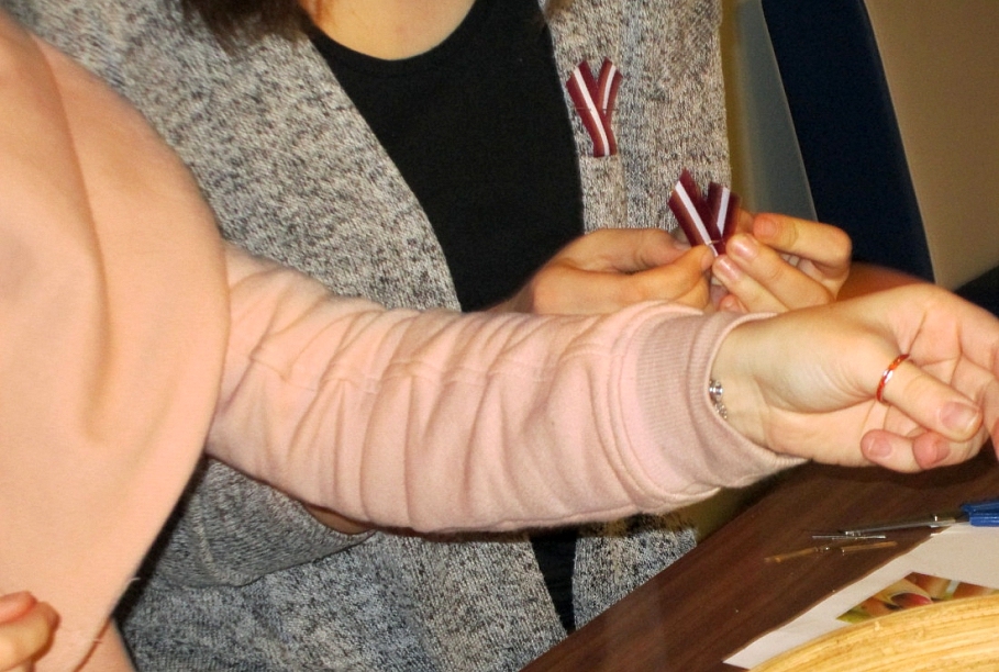 Aicina nēsāt pie apģērba sarkanbaltsarkanu lentīti